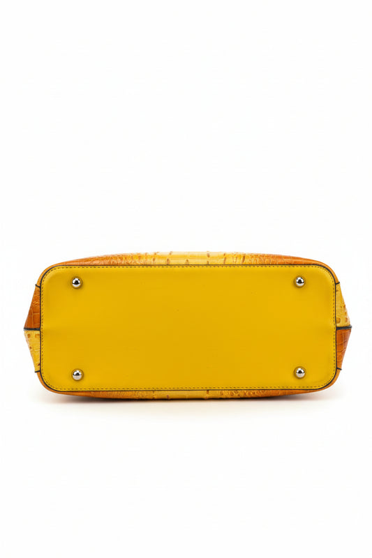 A close-up of a yellow handbag's bottom corner, showing a textured crocodile-embossed side panel and brass corner studs.